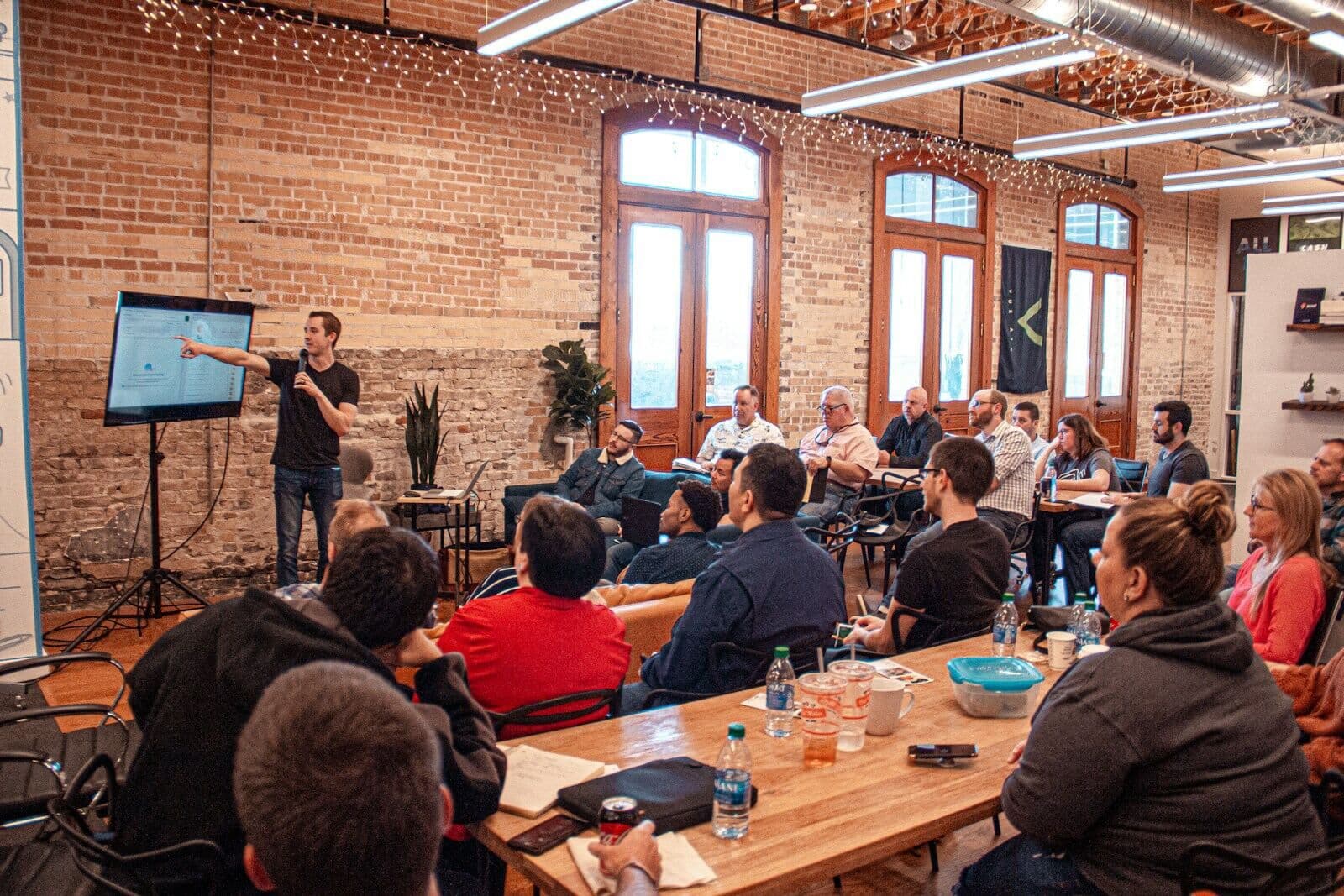 A facilitator presenting to a room of seated employees in a warm, brick-walled office